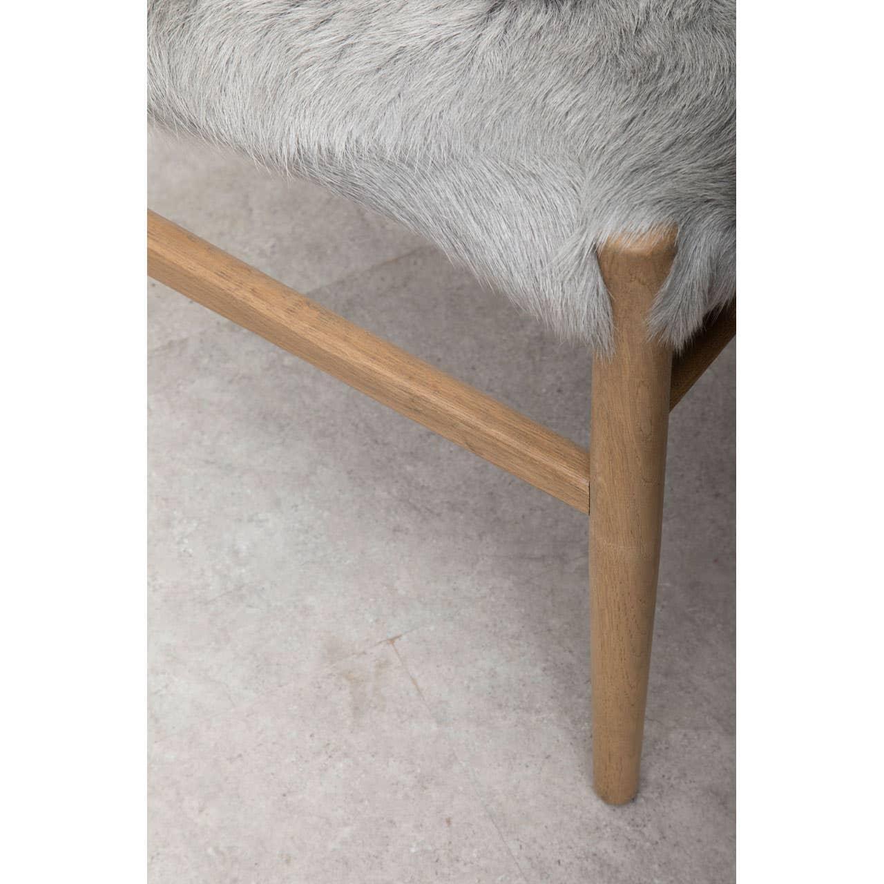 Close-up of wooden furniture leg with grey faux fur seat upholstery on stone floor