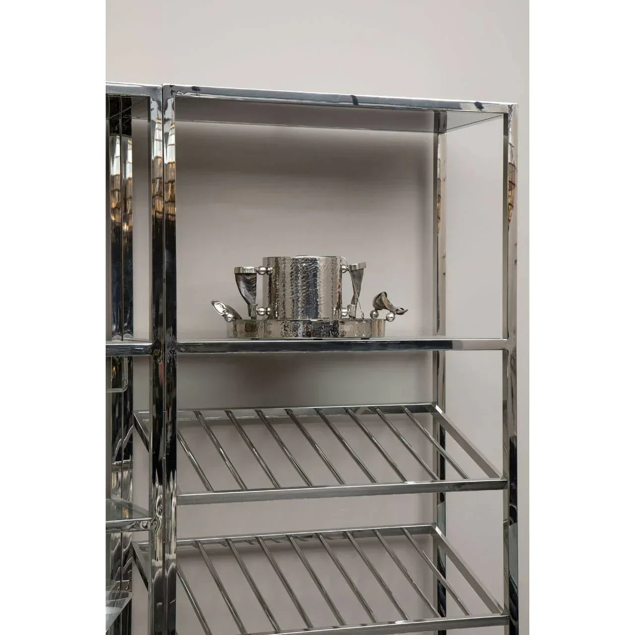 Chrome metal shelving unit with slatted shelves and decorative silver barware on top shelf