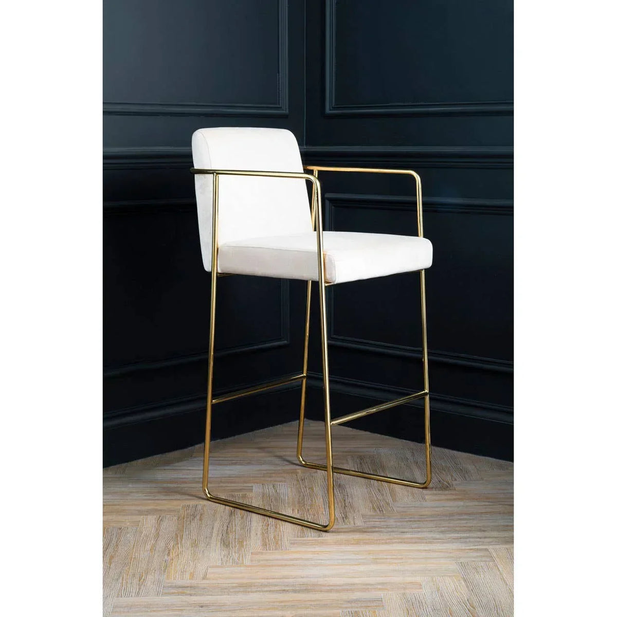 White bar stool with gold metal frame and arms on herringbone wood floor