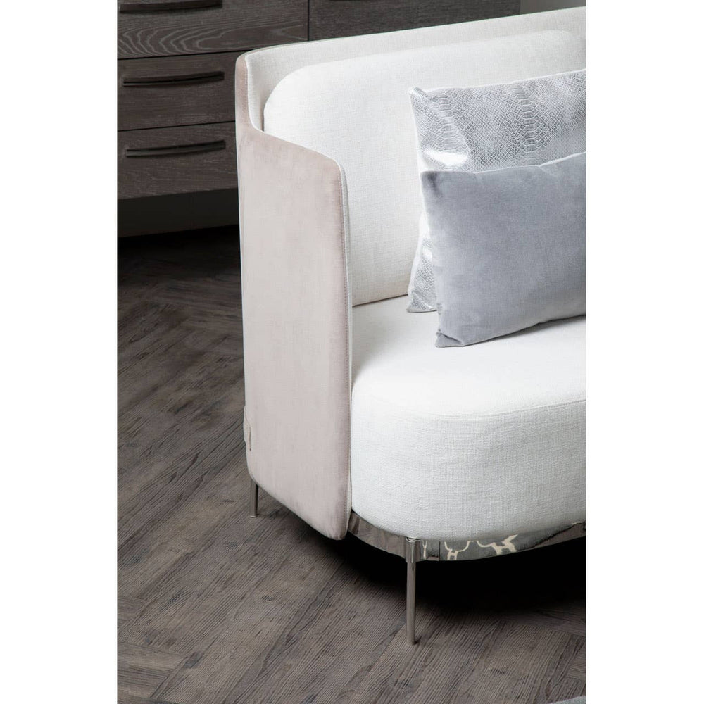 Ivory and mink two-seater sofa featuring a curved design with a soft, plush seat and a sleek, modern armrest. The sofa is complemented by a decorative gray pillow, set against a dark wooden floor