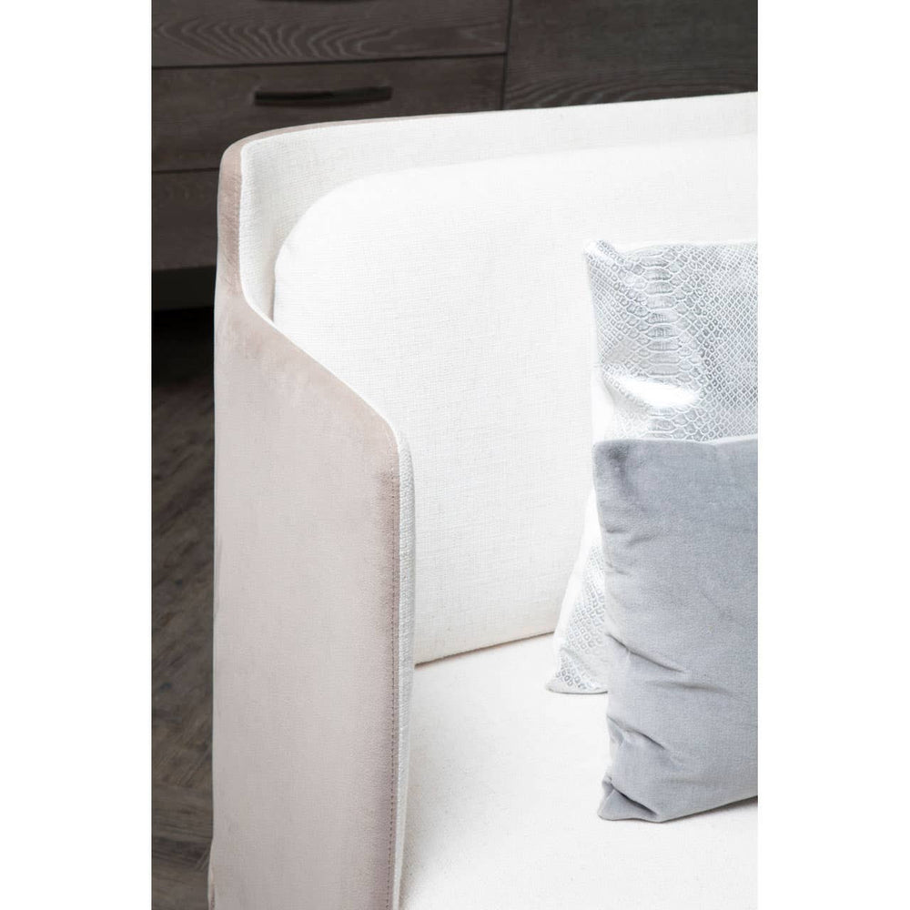 Ivory and mink two-seater sofa featuring a sleek, modern design with rounded edges and a soft fabric finish. A light blue decorative pillow is placed on the seat, complementing the neutral tones of the sofa. The background includes a dark wooden surface, suggesting a contemporary living space