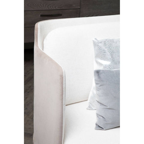Ivory and mink two-seater sofa featuring a sleek, modern design with rounded edges and a soft fabric finish. A light blue decorative pillow is placed on the seat, complementing the neutral tones of the sofa. The background includes a dark wooden surface, suggesting a contemporary living space