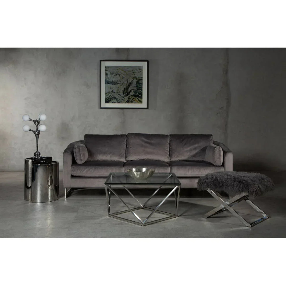 Grey velvet sofa with glass coffee table and chrome side table in modern living room setting