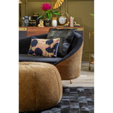 A leopard print pouffe in a warm brown color sits in a stylish living room setting, accompanied by a black and gold accent chair and a decorative pillow featuring a floral design. The background includes a wooden console table adorned with decorative items and a vibrant pink flower arrangement. The floor is covered with a textured rug, adding depth to the cozy atmosphere