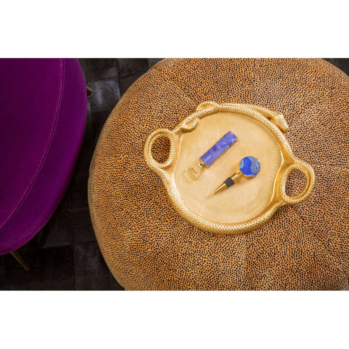 A leopard print pouffe in a warm, neutral tone, featuring a round shape and soft texture, with a decorative tray on top holding a blue object and a small tool, set against a dark background