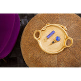 A leopard print pouffe in a warm, neutral tone, featuring a round shape and soft texture, with a decorative tray on top holding a blue object and a small tool, set against a dark background