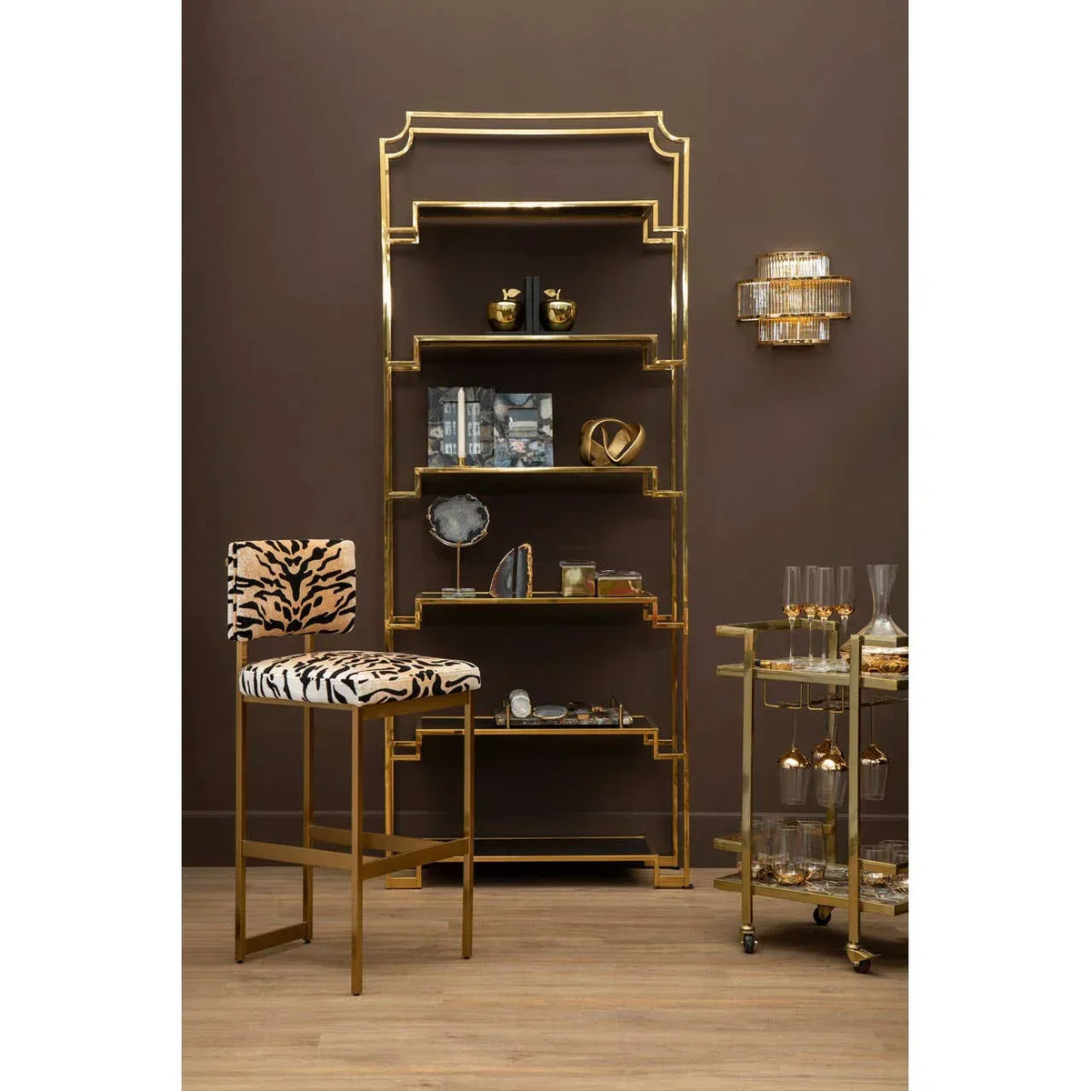Gold metal shelving unit with glass shelves, zebra print bar stool, bar cart and glassware