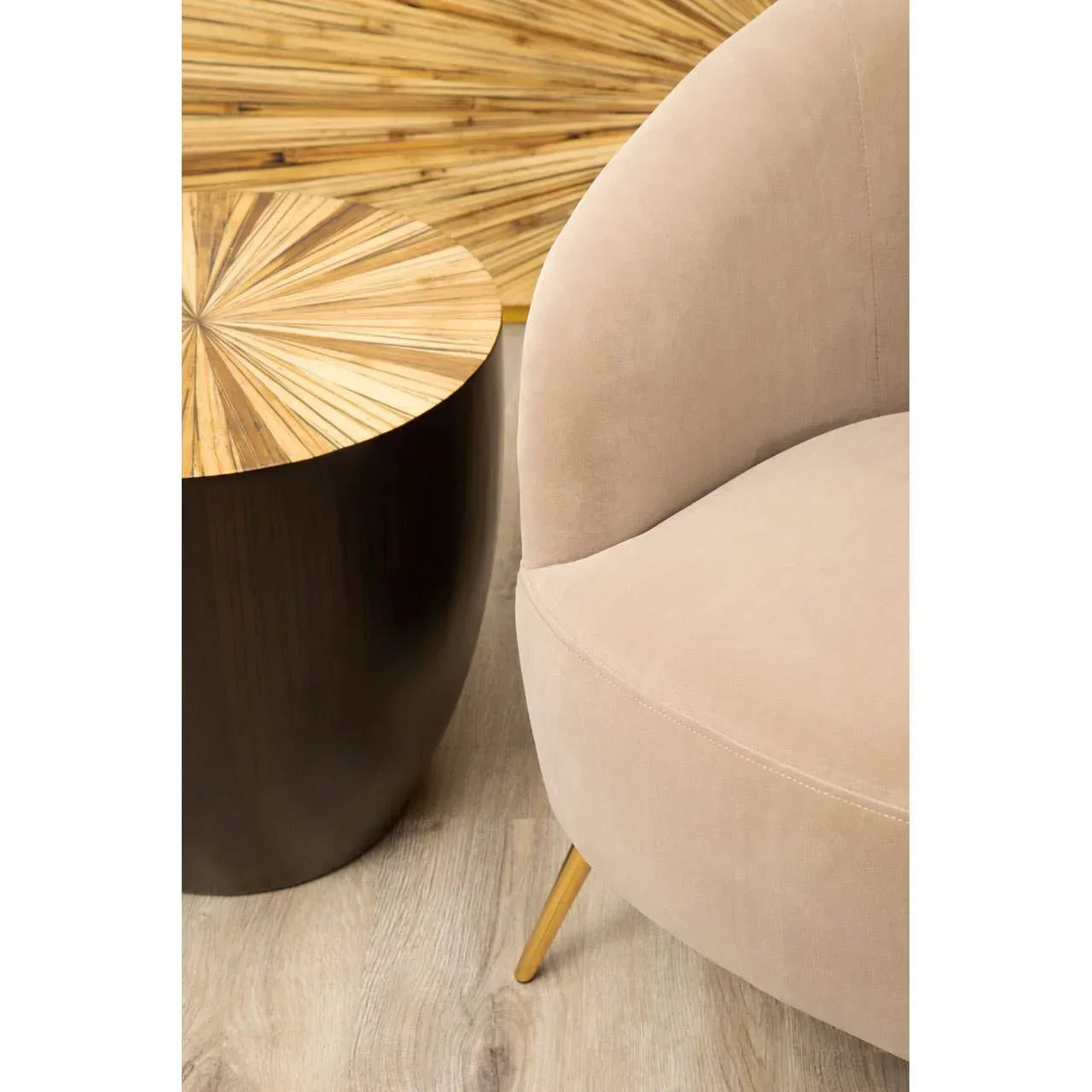 Beige curved accent chair with gold legs beside round wood side table on light flooring