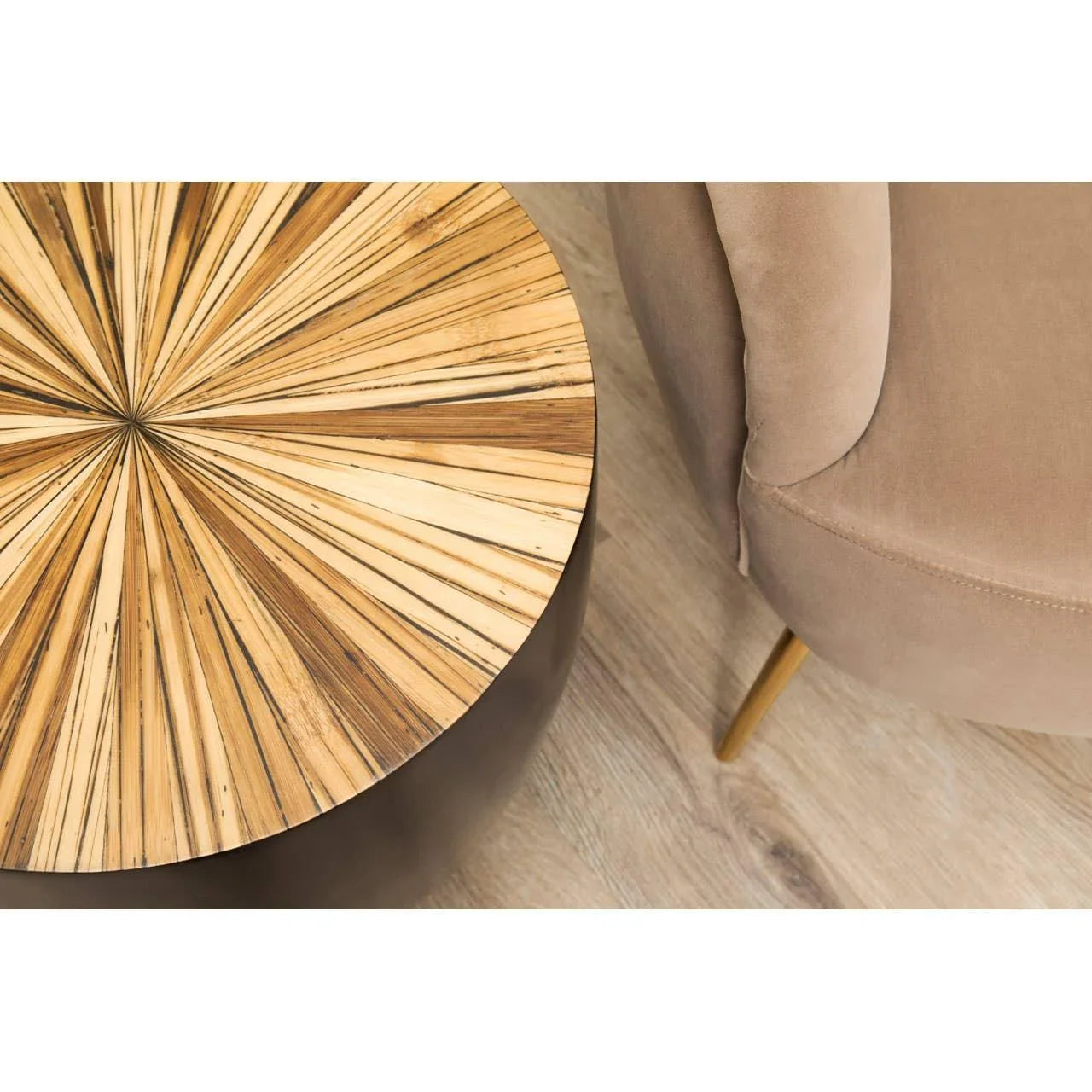 Round wooden accent table with sunburst pattern next to a beige velvet chair on wood floor