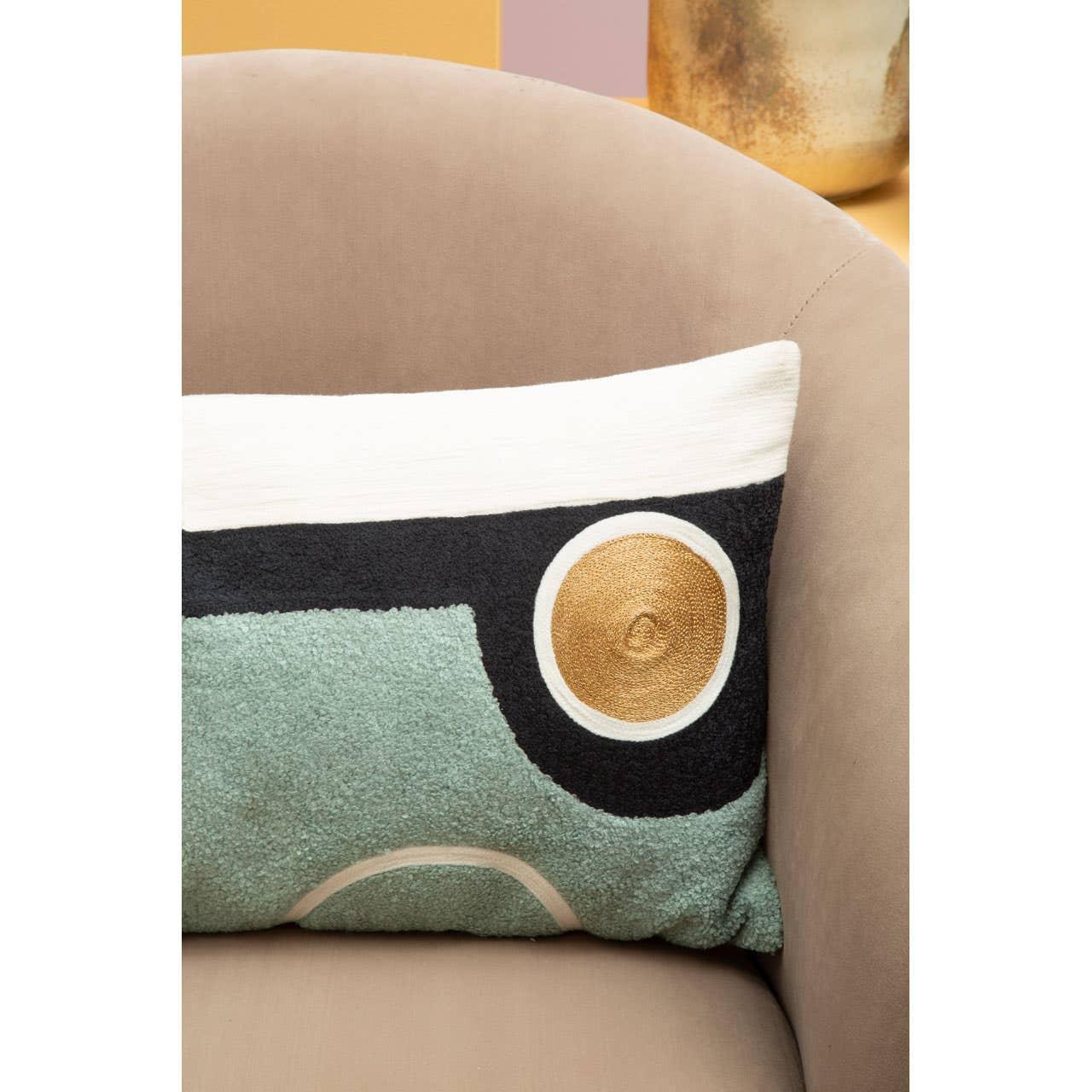 Abstract embroidered cushion on beige armchair, featuring teal, black, and gold detail