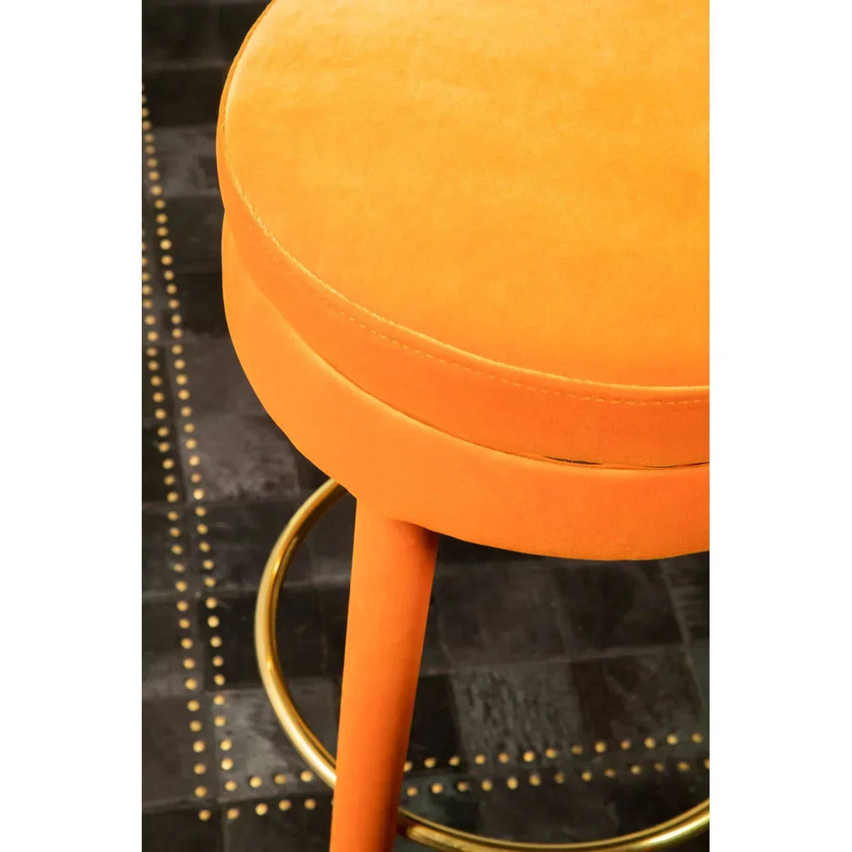 Orange velvet bar stool with gold footrest on black studded floor