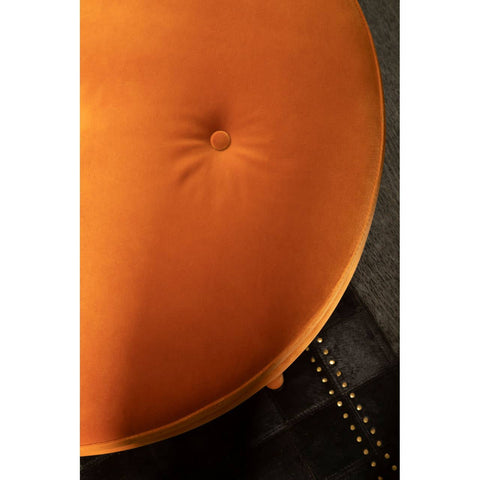 Round footstool upholstered in vibrant orange velvet with a tufted center, showcasing a smooth, soft texture. The footstool is positioned against a dark surface, highlighting its rich color and plush design