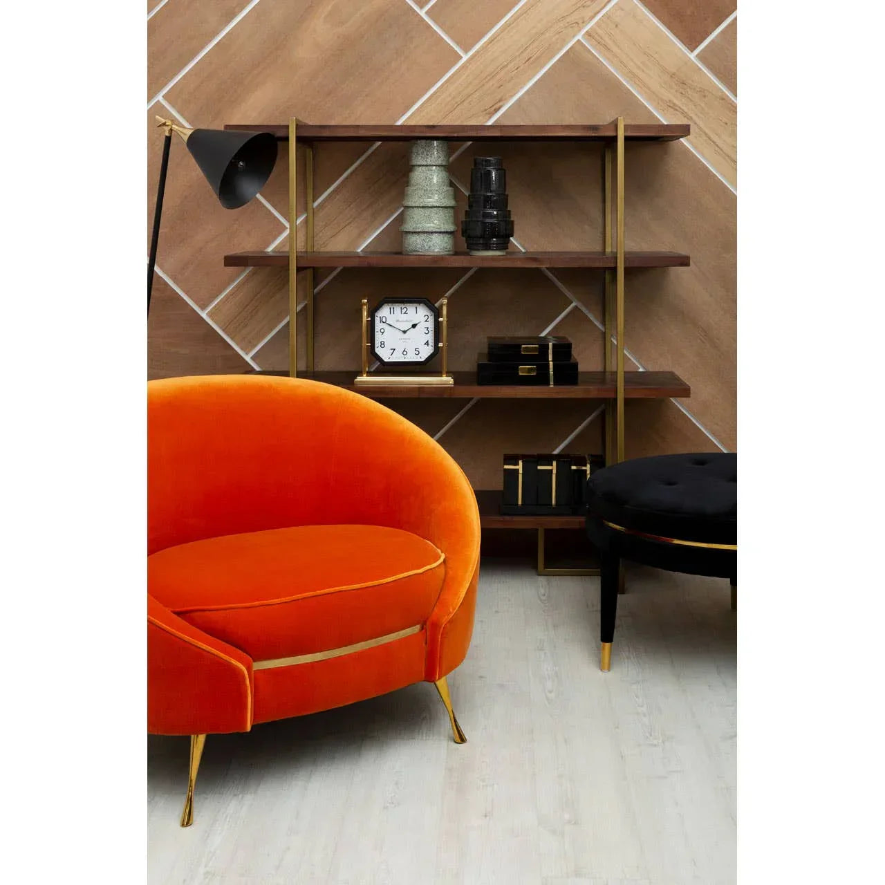 Orange velvet accent chair with gold legs beside modern shelving unit and black ottoman