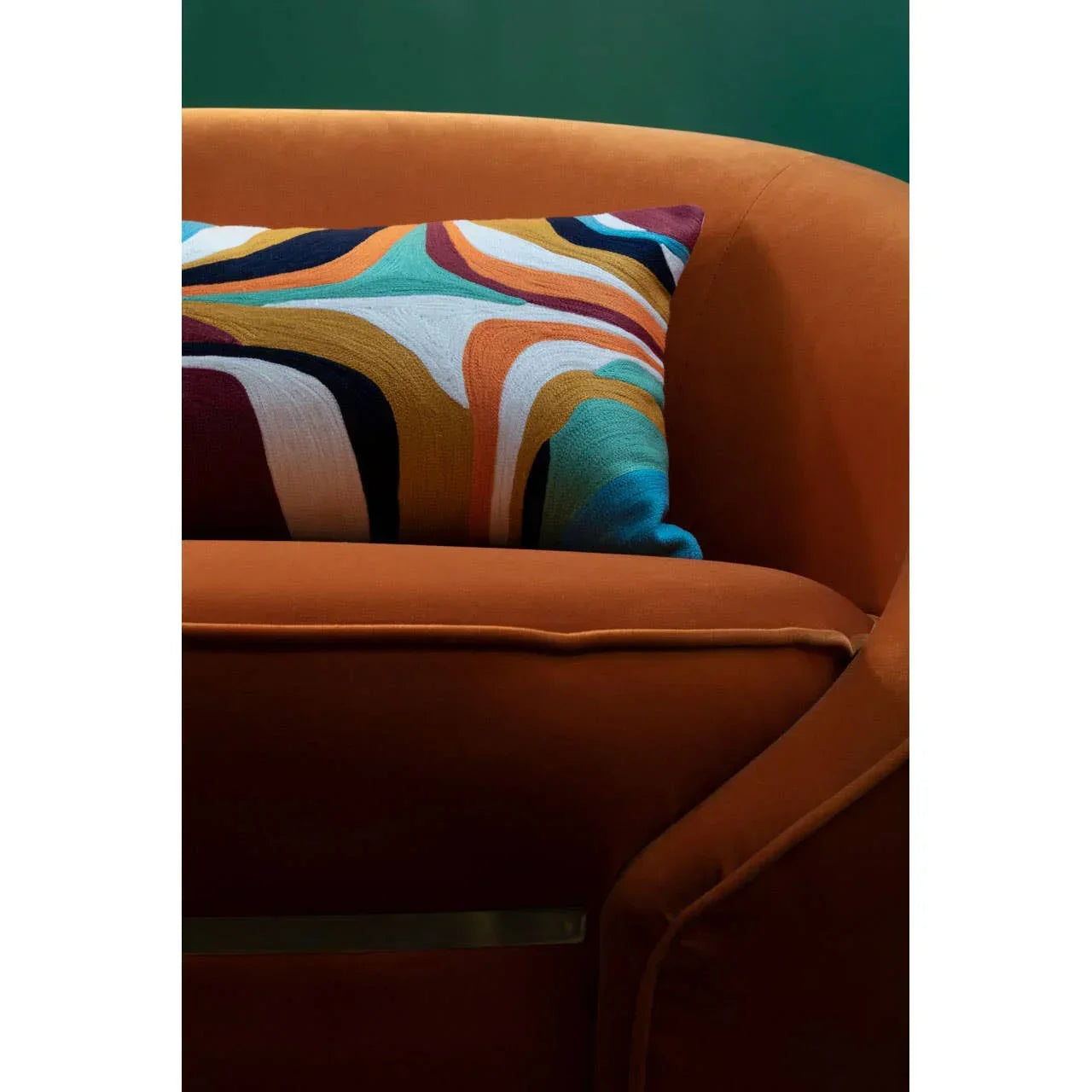 Burnt orange velvet sofa with multicoloured geometric cushion against green wall