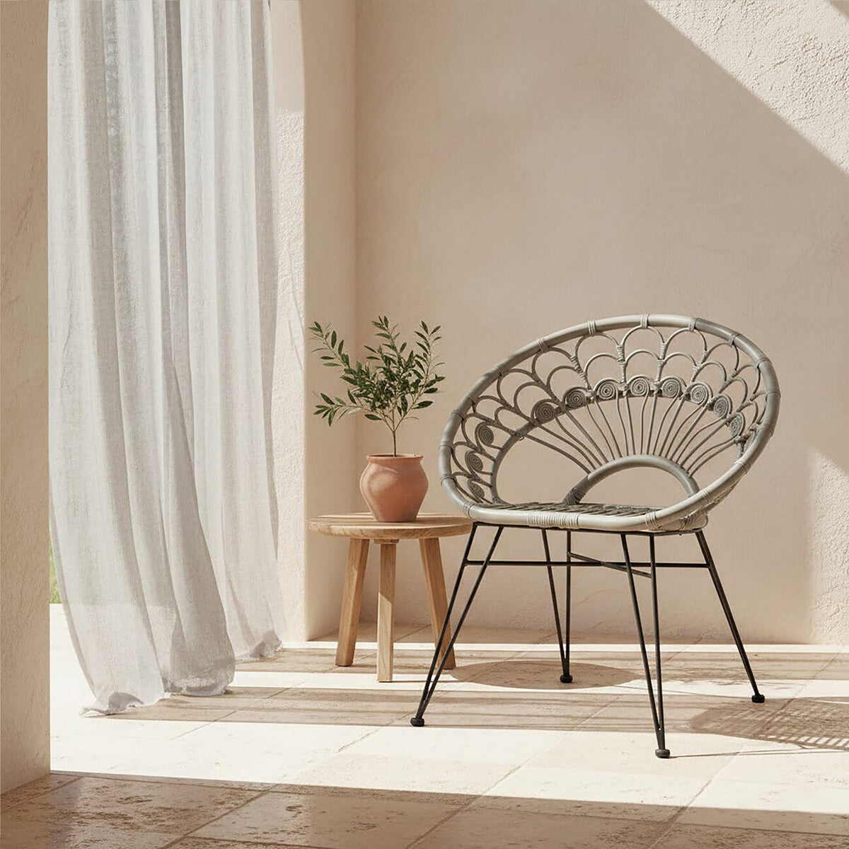 A grey natural rattan chair with a circular design sits beside a small wooden table, adorned with a potted plant. Soft, light-colored curtains drape in the background, and warm sunlight casts gentle shadows across the scene, creating a cozy atmosphere