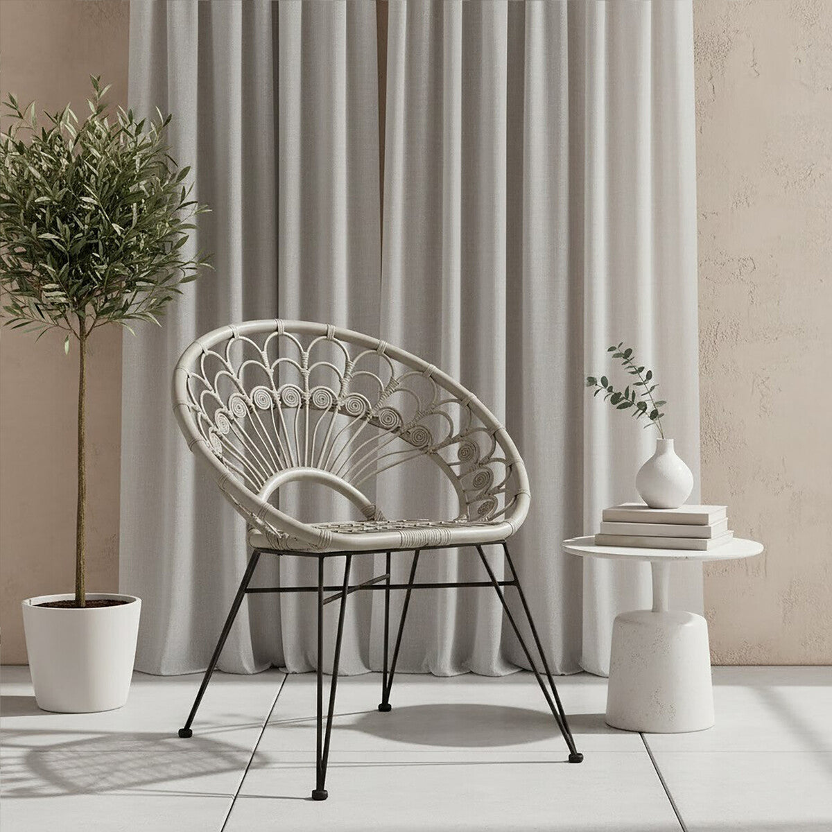 A grey natural rattan chair with a curved design sits next to a small white side table, adorned with a decorative plant and a stack of books. Light grey curtains drape in the background, complementing the neutral tones of the setting