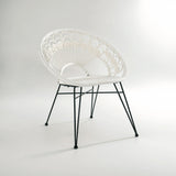 A stylish white rattan chair with a curved backrest and a natural woven texture, supported by sleek black metal legs, set against a light gray background