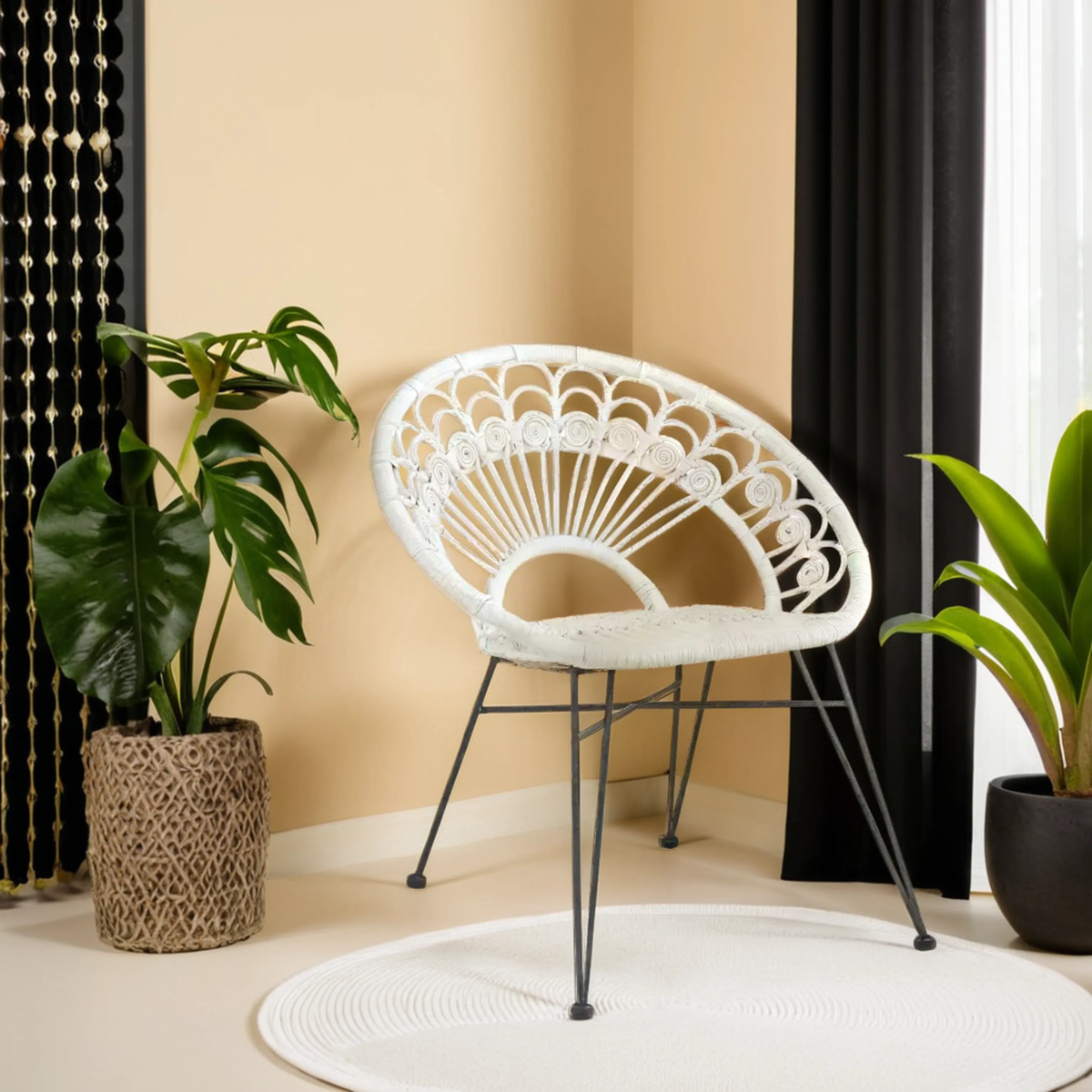 A white natural rattan chair with a circular backrest and black metal legs, positioned in a bright room with beige walls. A large green plant in a textured pot is nearby, and there is a round white rug on the floor. Black curtains frame a window, adding contrast to the light space