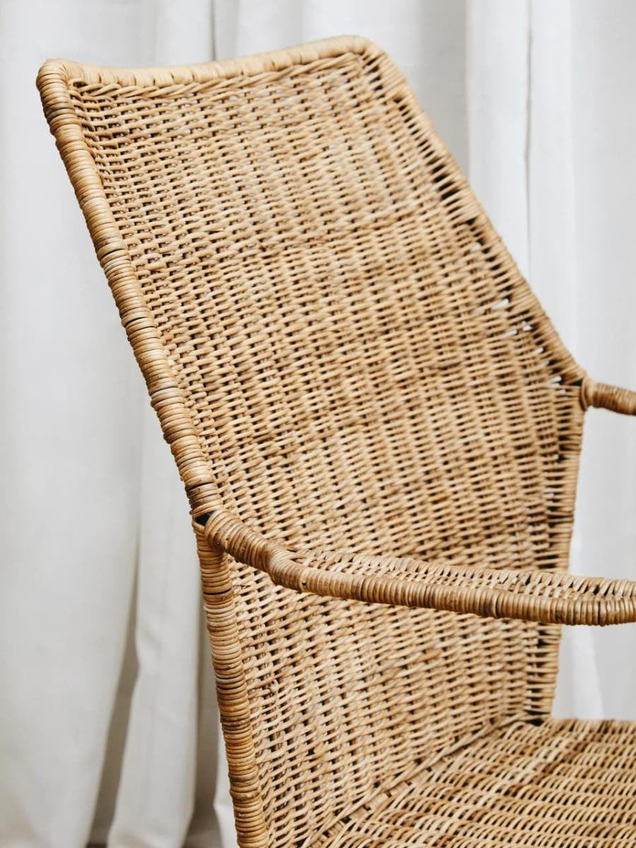 Natural rattan chair with an angled design, featuring a woven texture and light brown color, positioned against a light-colored backdrop. The chair has a high backrest and armrests, showcasing its modern and minimalist style