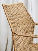 Natural rattan chair with an angled design, featuring a woven texture and light brown color, positioned against a light-colored backdrop. The chair has a high backrest and armrests, showcasing its modern and minimalist style