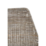 Close-up view of the angled design of a natural rattan chair, showcasing the textured weave and the smooth, curved edge. The chair features a neutral color palette that highlights the natural fibers