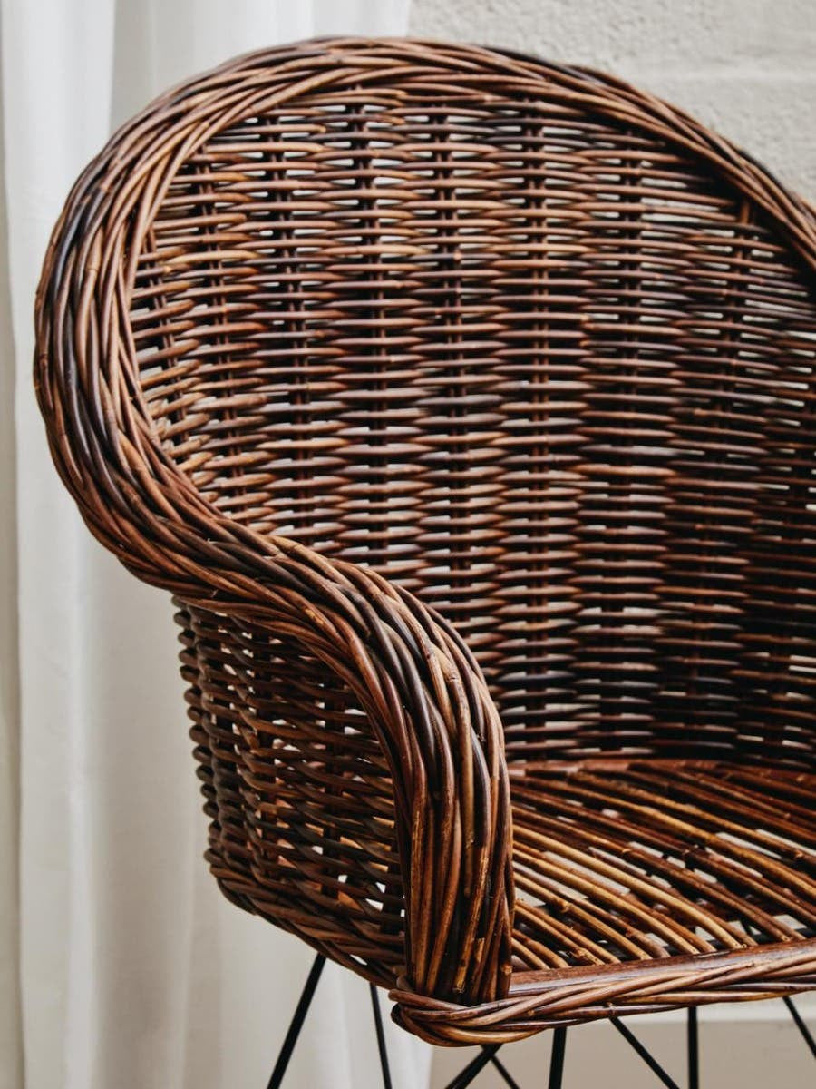Natural rattan chair with a curved backrest and woven texture, featuring a rich brown color and a sturdy metal base. The chair's design highlights the intricate weaving of the rattan, showcasing its organic aesthetic