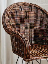 Natural rattan chair with a curved backrest and woven texture, featuring a rich brown color and a sturdy metal base. The chair's design highlights the intricate weaving of the rattan, showcasing its organic aesthetic