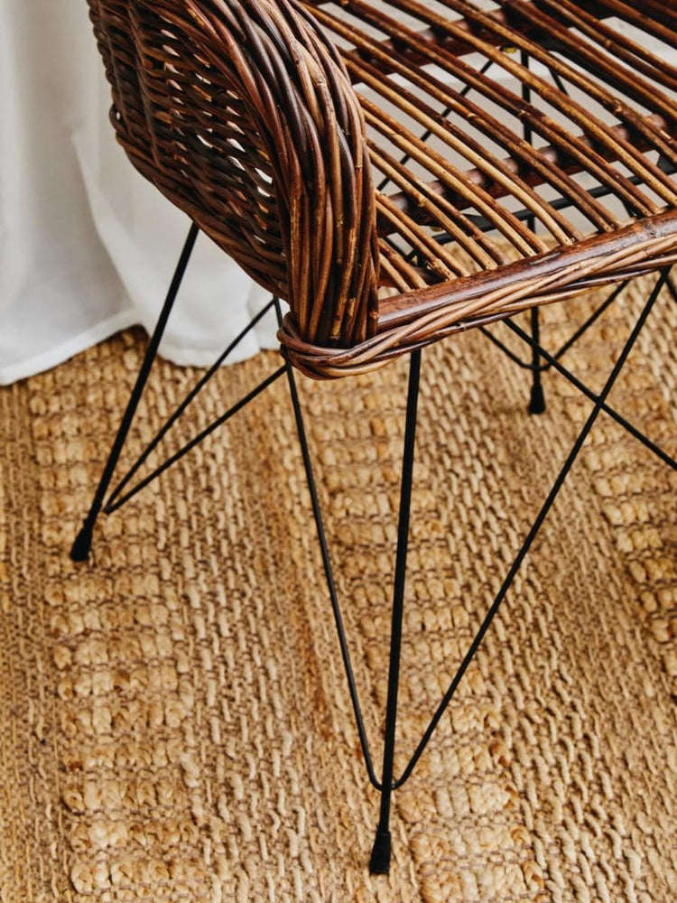 Natural croco rattan chair with a woven seat and backrest, supported by sleek black metal legs, placed on a textured woven rug