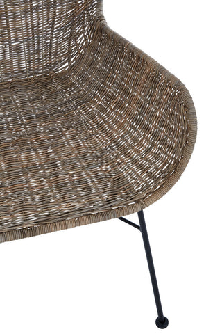 Curved seat of a natural rattan chair with a textured surface, supported by slender black metal legs. The design showcases a warm, earthy tone and a modern aesthetic suitable for home decor