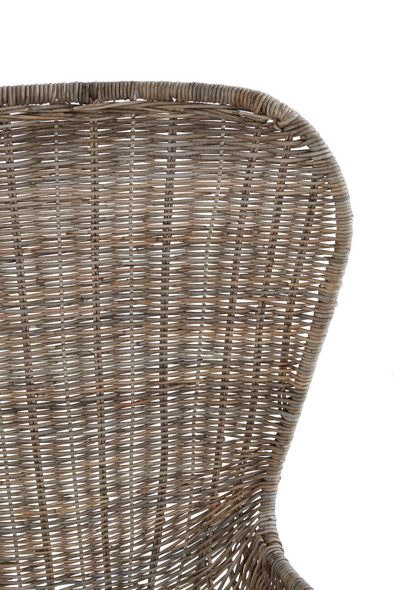 Curved backrest of a natural rattan chair showcasing intricate weaving patterns and a warm, earthy tone. The chair's design emphasizes a smooth, organic shape, highlighting the texture of the rattan material