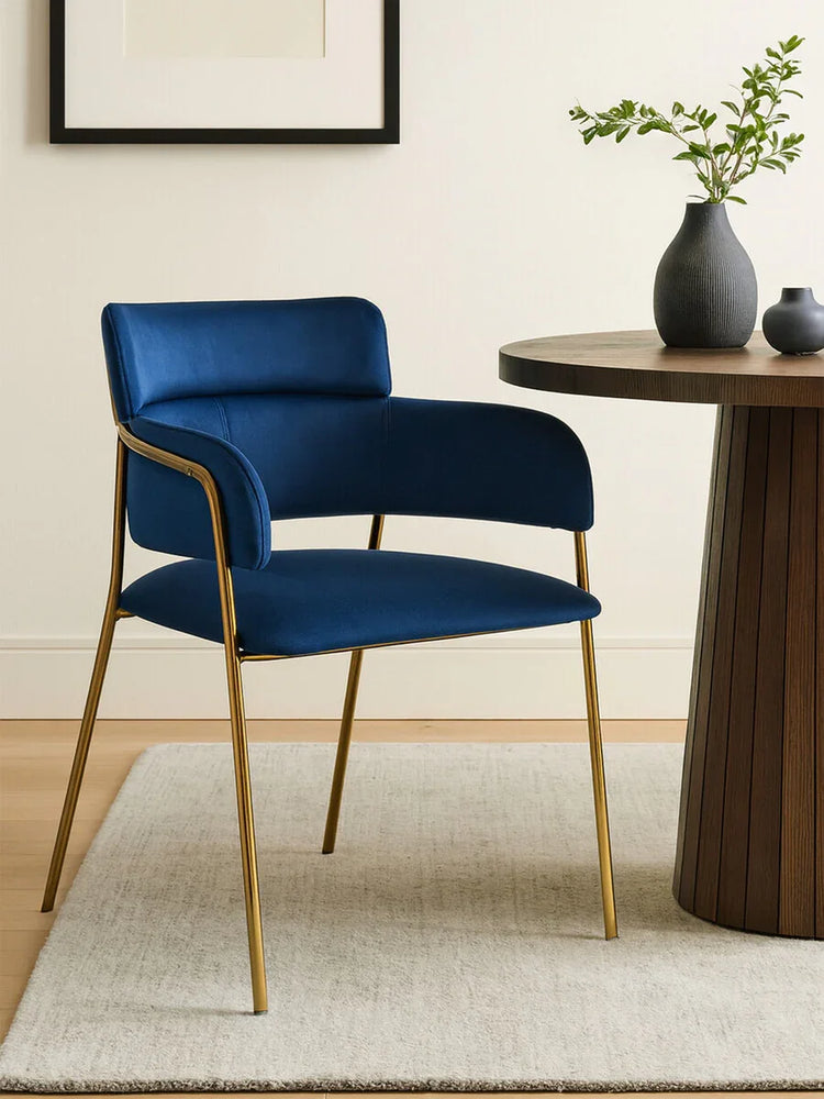 Blue velvet dining chair with gold legs beside round wooden table on light rug