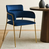 Blue velvet dining chair with gold metal legs beside round wooden table on cream rug