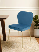 Blue velvet dining chair with gold metal legs beside wooden table on textured rug