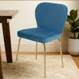 Blue velvet dining chair with gold metal legs beside wooden table on patterned rug