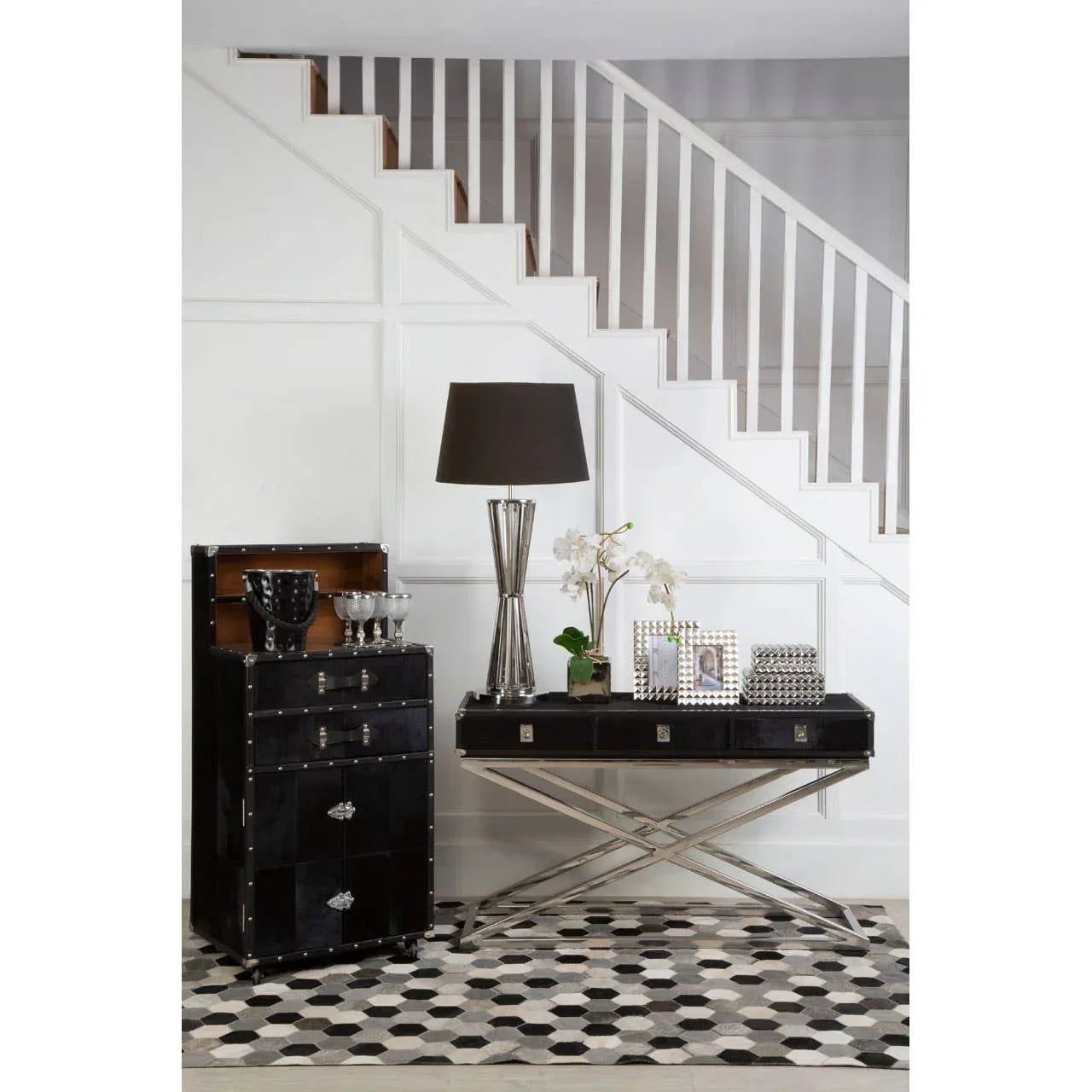 Black hallway console table and cabinet with silver lamp, decor, and geometric rug under stairs