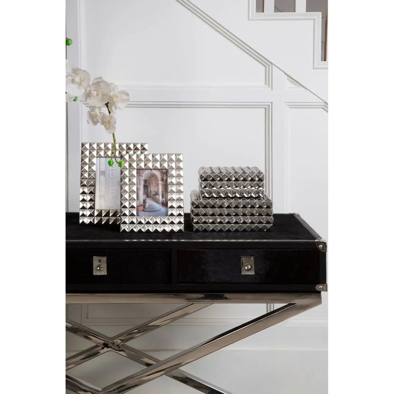 Silver geometric photo frames and boxes on black console table under staircase