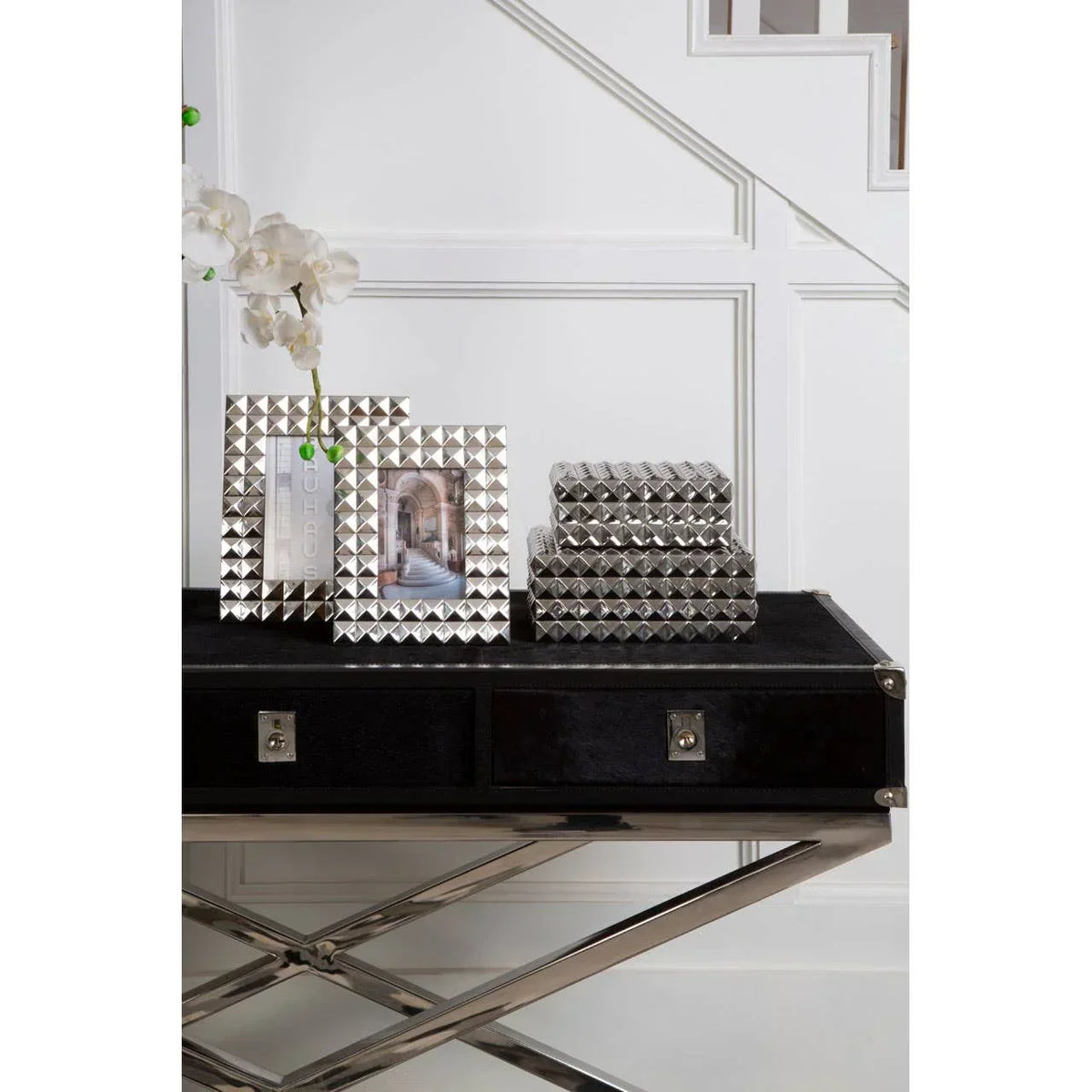 Silver geometric photo frames and boxes on black console table under staircase