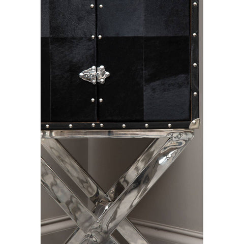 A sleek drinks cabinet featuring a hair-on leather front with a glossy black finish, adorned with decorative studs and a crystal-like handle. The cabinet is supported by a modern cross base made of clear acrylic, adding a contemporary touch to the overall design