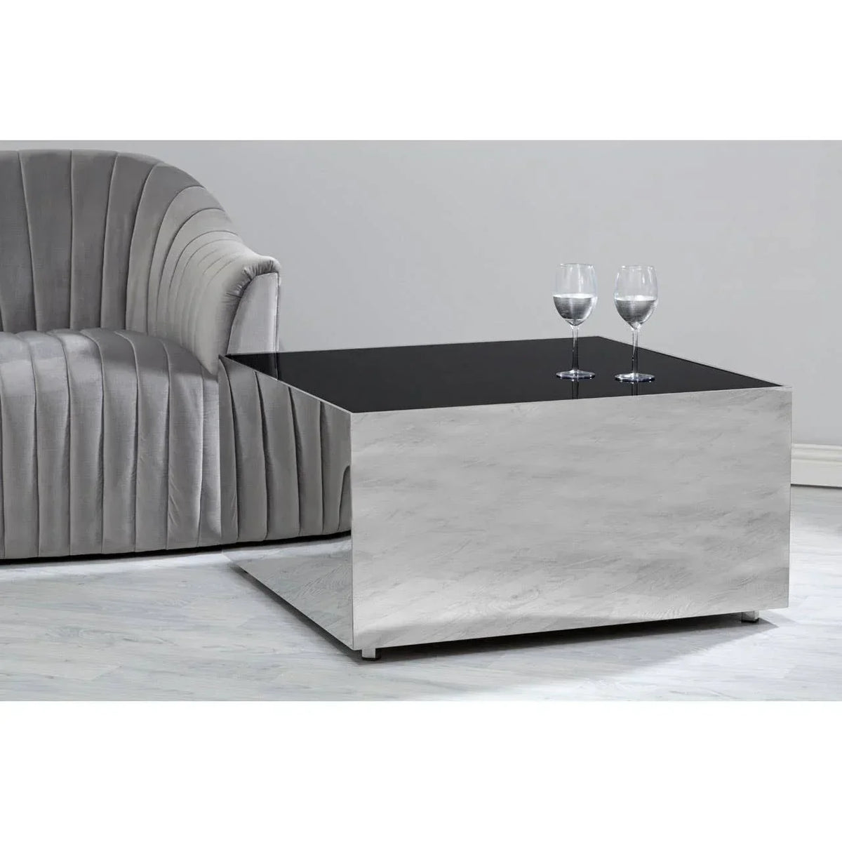 Modern square coffee table with black glass top beside grey velvet sofa in living room setting