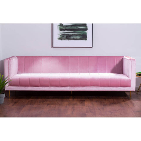 A three-seat sofa upholstered in soft pink fabric, featuring a sleek and modern design with clean lines and minimalistic armrests. The sofa is positioned on a wooden floor, complemented by a wall with a framed artwork above it
