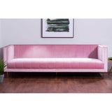 A three-seat sofa upholstered in soft pink fabric, featuring a sleek and modern design with clean lines and minimalistic armrests. The sofa is positioned on a wooden floor, complemented by a wall with a framed artwork above it
