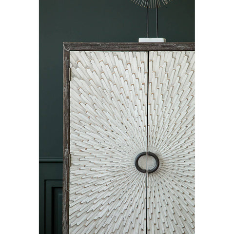 Milan Two Door Elm Wood Wine Cabinet featuring a textured front with a circular handle, set against a dark green wall. The cabinet showcases a natural wood finish with intricate patterns, emphasizing its elegant design