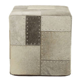 Square pouffe featuring a patchwork design in various shades of grey and beige, with visible stitching details. The surface appears soft and textured, suitable for use as a footrest or additional seating