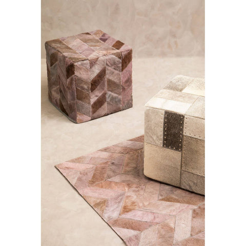 A textured grey pouffe with a geometric design sits on a light-colored floor, accompanied by a similarly styled pouffe in a warm, earthy tone. The background features a smooth, neutral wall that complements the furniture