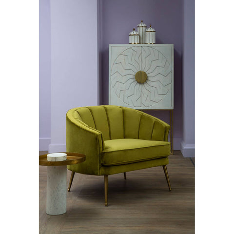 A stylish yellow accent chair with a curved backrest and wooden legs is positioned next to a small round side table. Behind the chair, a white wash mango wood cabinet features a textured front with a circular handle, set against a soft purple wall. The floor is a light wood finish, adding warmth to the scene