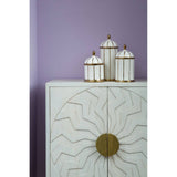 White wash mango wood cabinet featuring a sunburst design on the front, with two doors and a round brass handle. On top of the cabinet, three decorative jars with white and gold accents are arranged against a soft purple wall