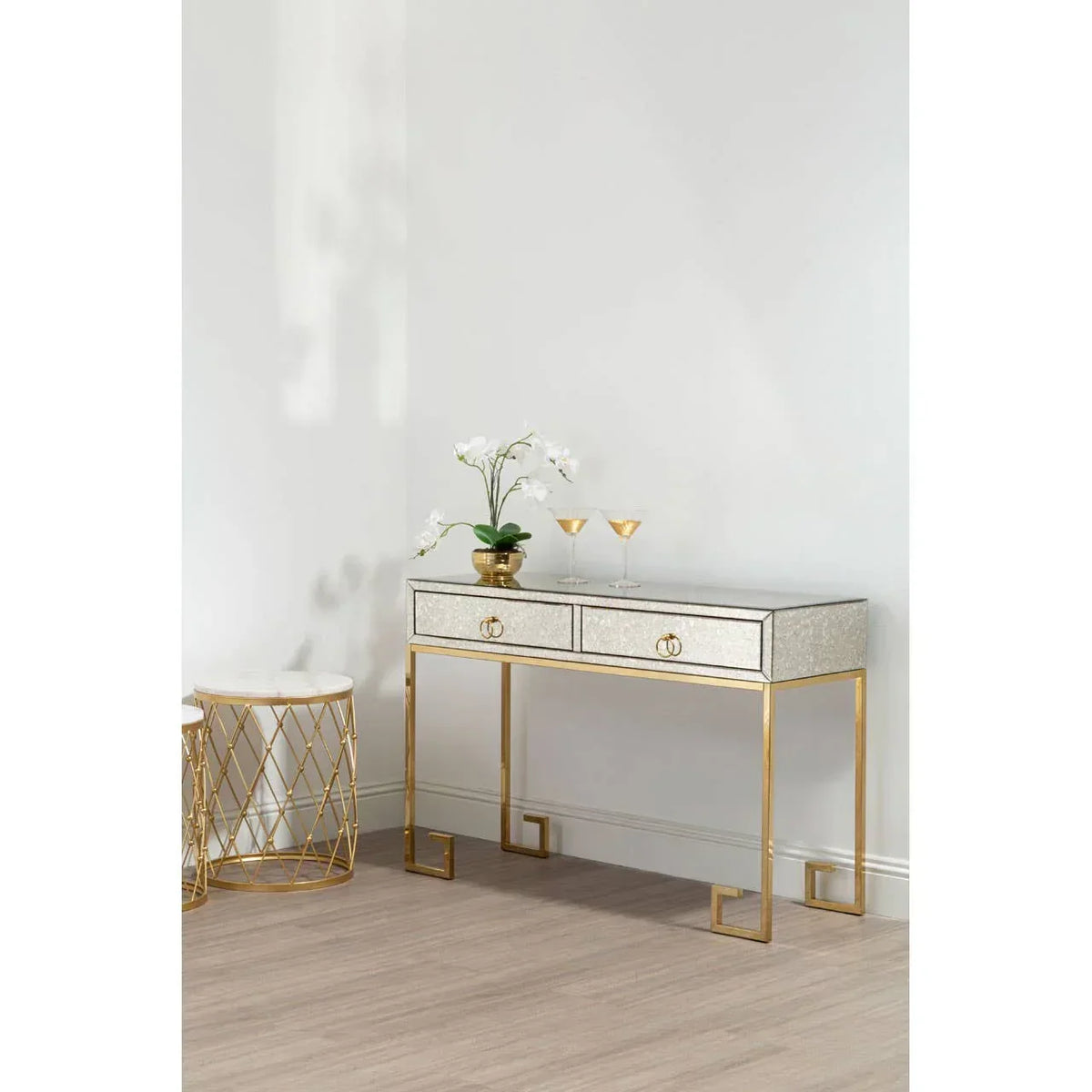 Mirrored console table with gold frame, two drawers, orchid plant, and drinks in modern room