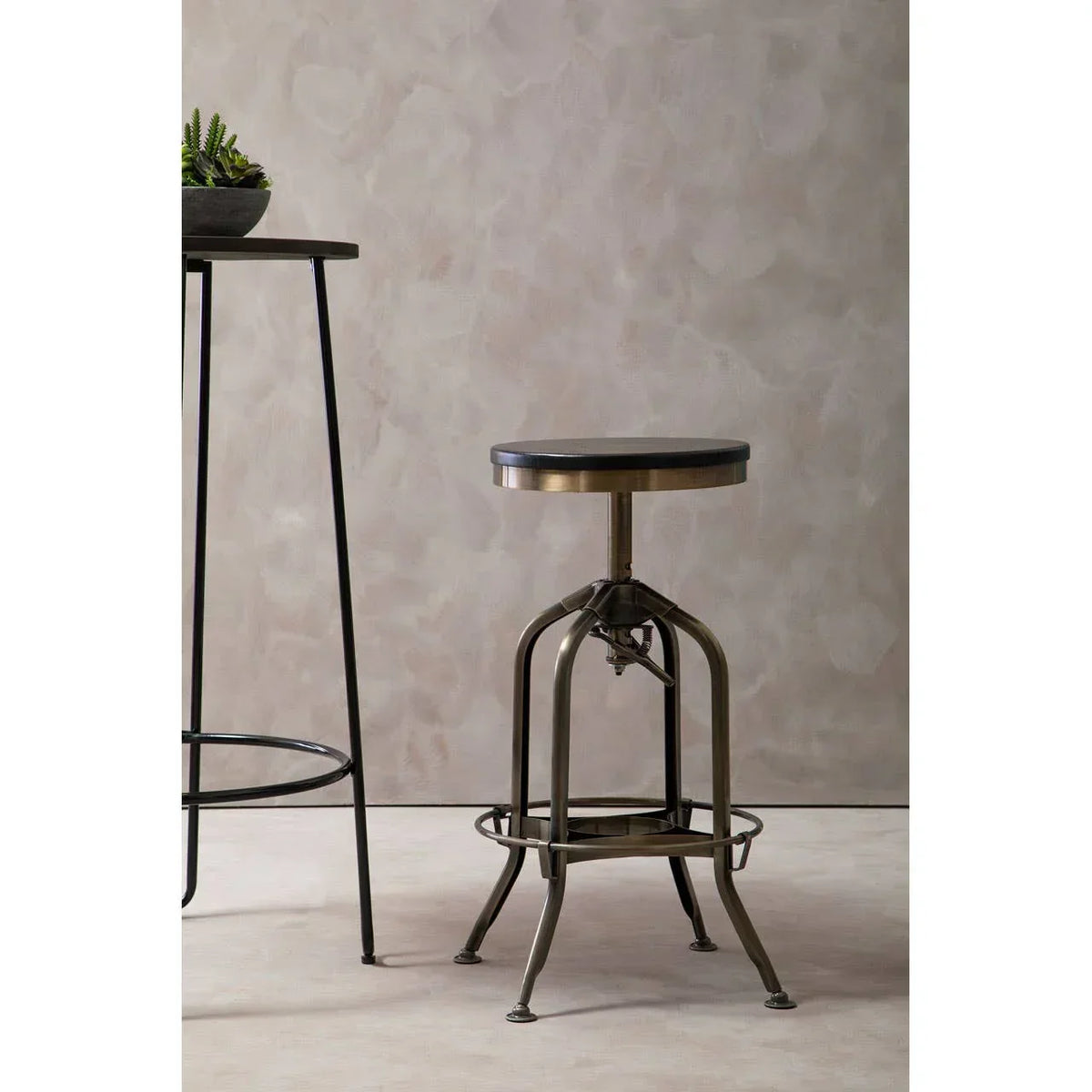 Industrial metal bar stool with round wooden seat beside tall black bar table