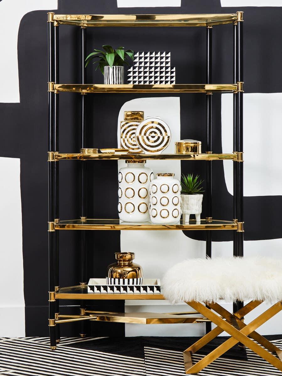 Black and gold shelving unit with decorative vases, plant, and geometric tray in modern room