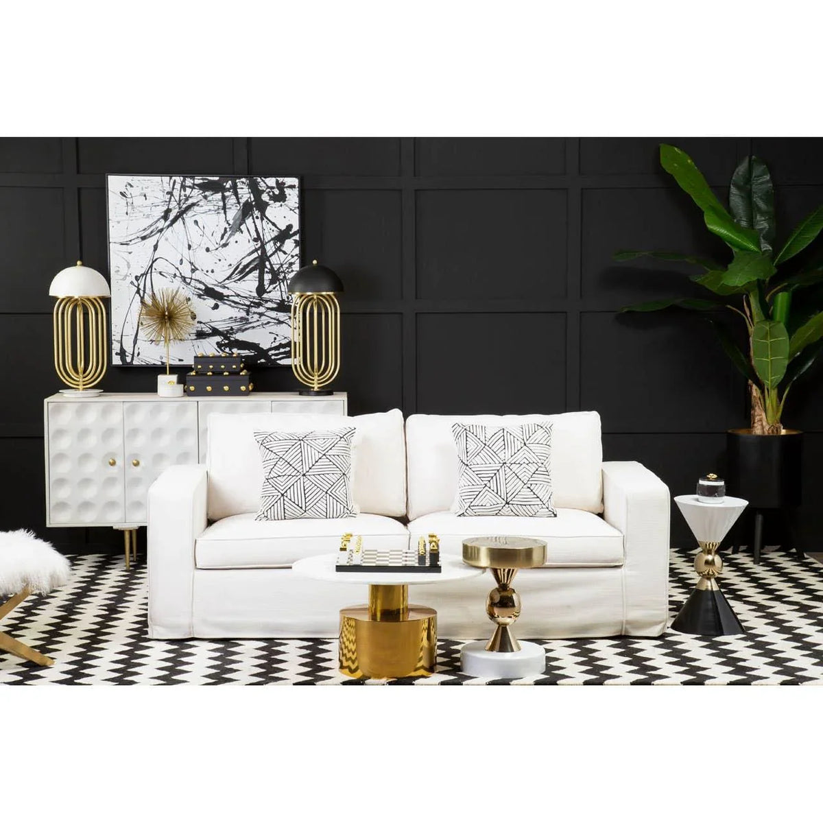 Modern living room with white sofa, geometric cushions, gold accent tables, black wall